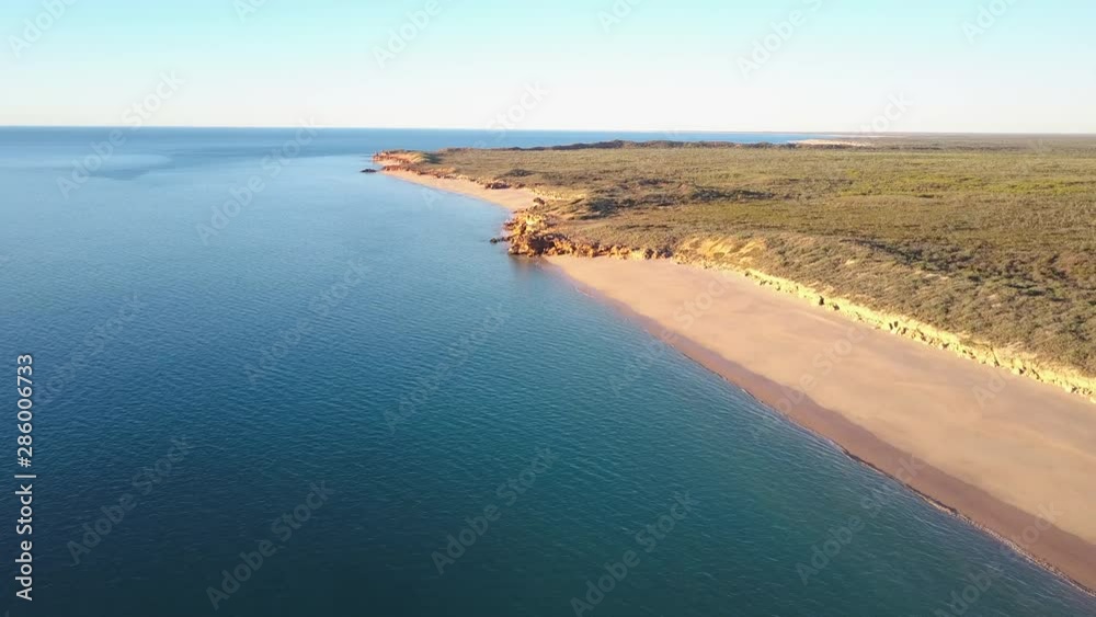 Scenic panoramic aerial drone view of flight high above ocean and remote beach in Western Australia, with rocky cliff coastline, summer sunny blue sky and horizon as background and copy space. Scenic panoramic aerial drone view of flight high above ocean and remote beach in Western Australia, with rocky cliff coastline, summer sunny blue sky and horizon as background and copy space.