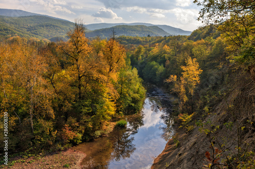 View from steep bank of Afips river at sunset. Scenic sunny golden autumn landscape of Caucasus Mountain forest at Seversky district, Krasnodar region, West Caucasus, Russia.