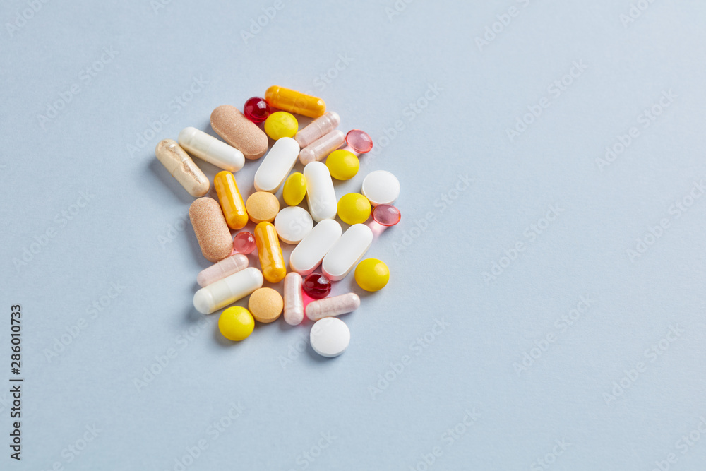 Multicolor vitamins and supplements on bright paper background. Concept for a healthy dietary supplementation. Top view. Copy space. Multicolor vitamins and supplements on bright paper background. Concept for a healthy dietary supplementation. Top view. Copy space.