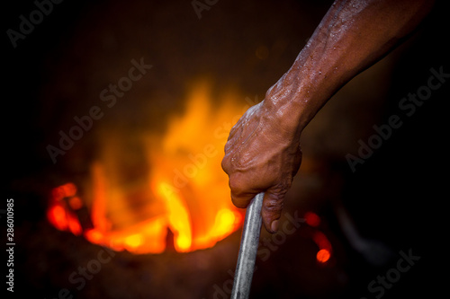Unsafe worker hands. A local steel machine parts making yard worker melting scrap on hot furnace.
