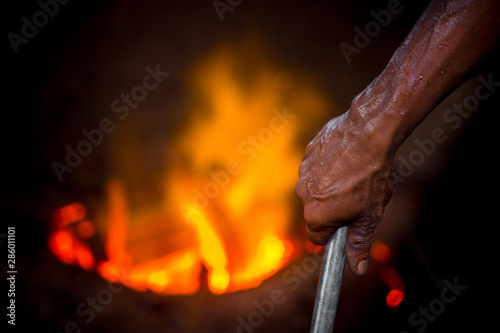 Unsafe worker hands. A local steel machine parts making yard worker melting scrap on hot furnace.