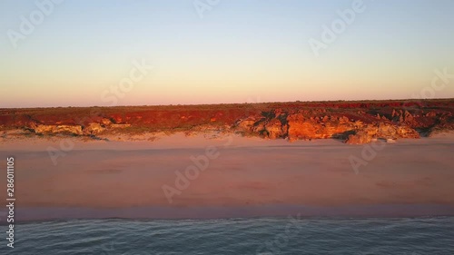 Scenic panoramic aerial drone view of people walking on remote beach in Western Australia at sunset, with rocky cliff coastline, colorful twilight sky and horizon as background and copy space.