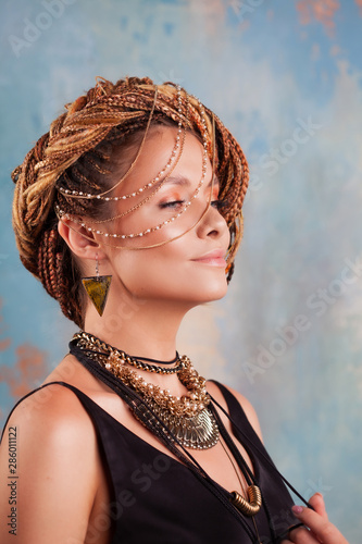 Southern flavor. Portrait of a luxurious tanned woman, pensive, stylish, with an exotic hairstyle and large jewels.