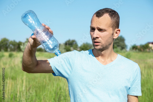 young man outdoors with frustration looks at an empty water bottle