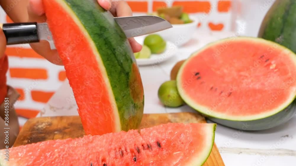 close up hand using small knife sliced water melon into piecs on the cutting board. Watermelon is a fruit that has cool properties. Will help reduce pain, fever, dry throat, relieve mouth sores Boil t close up hand using small knife sliced water melon into piecs on the cutting board. Watermelon is a fruit that has cool properties. Will help reduce pain, fever, dry throat, relieve mouth sores Boil t