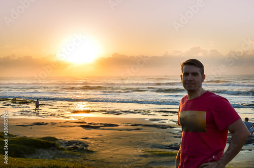 Young man with red shirt having the sunrise on a beach in the background.
