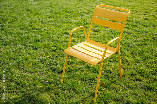 yellow metal chair stands on a lawn with green grass