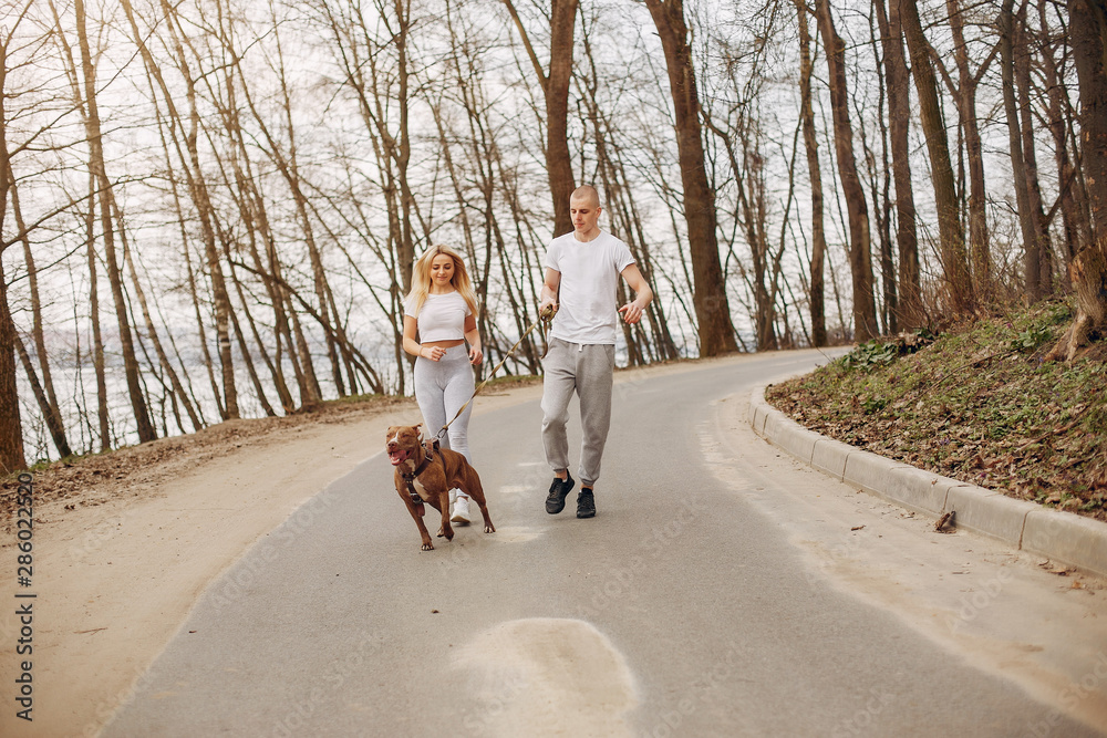 Beautiful couple in a park. Sportsman in a sportswear. Couple with a dog Beautiful couple in a park. Sportsman in a sportswear. Couple with a dog