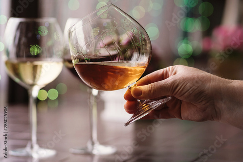 Swirl the drink this is moment when you must see socalled legs on the glass. Snifter of brandy in elegant glass with space for text on colorful background. Two glasses of wine in background unfocus