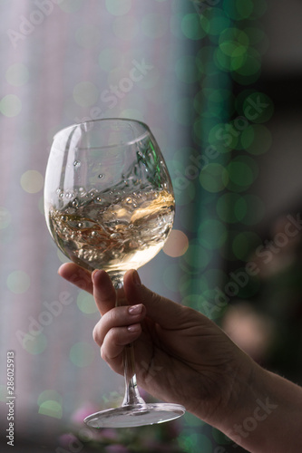 Hand sommelier holding glass of white wine. Swirling wine glass in wine tastings White wine concept. Wine tour. Vertical, cold toning