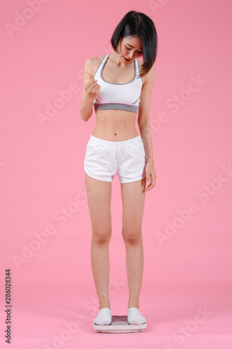 Healthy woman standing on weight scales in home on pink backgrounds, Healthy concept, Diet concept © I Believe I Can Fly