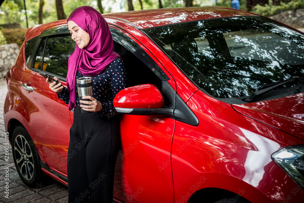 Muslim Female with her smartphone beside her car. Car insurance concept.