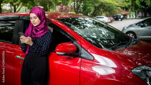 Muslim Female with her smartphone beside her car. Car insurance concept.