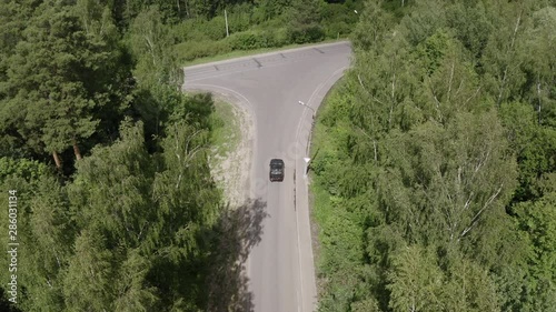 Black car driving on countryside road past green trees in summer forest. Drone view car turning reverse on asphalt road in countryside. Car tourism at summer holiday photo