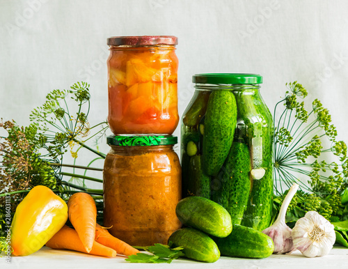 Fermented preserved or canning various vegetables zucchini carrots cucumbers in glass jars on table a light background.