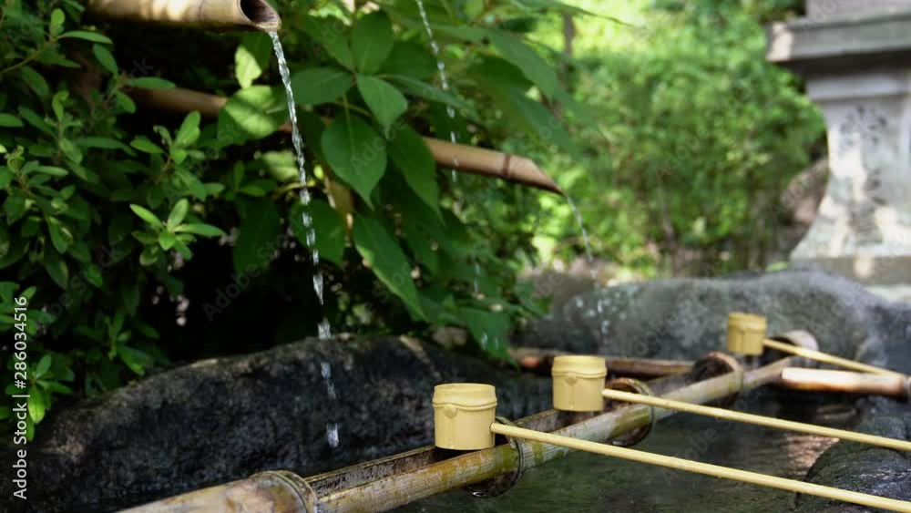 4K Medium shot of bamboo ladle on rock basin with leaking water from bamboo pipe in tranquil garden at japanese temple. Woman hand washing hand before go into shinto shrine, Tokyo, Japan 4K Medium shot of bamboo ladle on rock basin with leaking water from bamboo pipe in tranquil garden at japanese temple. Woman hand washing hand before go into shinto shrine, Tokyo, Japan