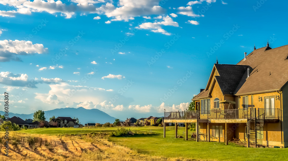 Obraz premium Panorama Scenic landscape with homes on a grassy terrain under blue sky and clouds