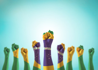Brazil flag on people hands with clenched fists raising up for labor day national holiday celebration and stay strong for Brazilian power isolated on blue sky background (clipping path)