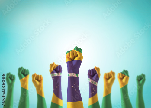 Brazil flag on people hands with clenched fists raising up for labor day national holiday celebration and stay strong for Brazilian power isolated on blue sky background (clipping path) photo