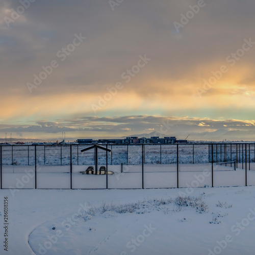 Square frame Tennis courts inside a chain link fence and blanketed with snow in winter © Jason