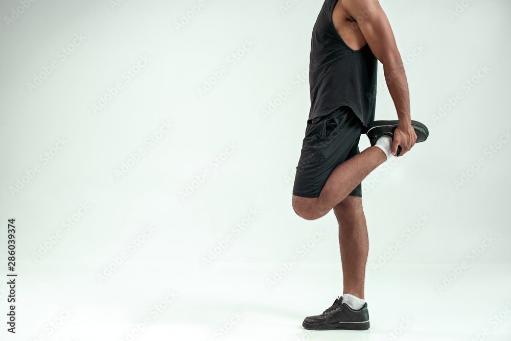 Great shape. Cropped photo of afro american man stretching his leg while standing against grey background