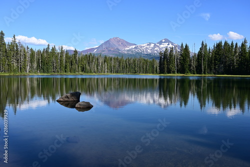 Fototapeta Naklejka Na Ścianę i Meble -  Middle and North Sisters volcanoes reflected in the still water of Scott Lake on a clear and sunny summer afternoon.