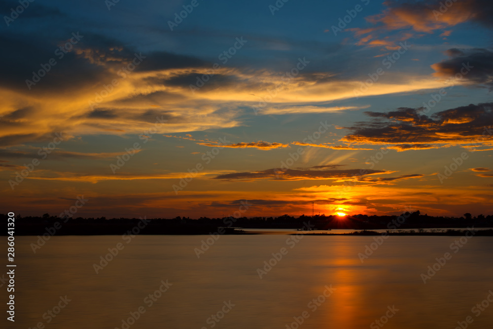 Beautiful Sunset in the sky with sky blue and orange light of the sun through the clouds in the sky, Orange and red dramatic colors over the lake. - Image