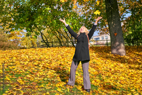 Middle-aged blonde in an autumn park throws fallen leaves to the top