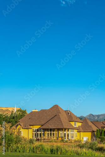 Facade of house with yellow wall balcony and brown roof against rich blue sky © Jason