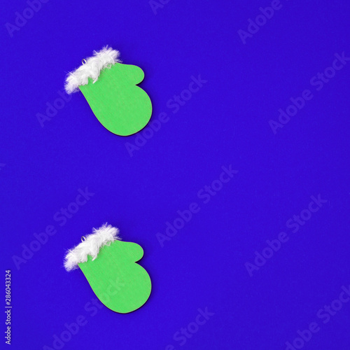 Small wooden christmas toy Green mittens on bluepaper background with copy space. Flat lay for winter holiday concept. photo