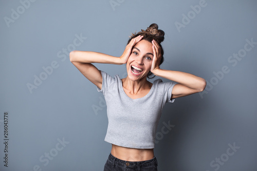 Portrait of an enthusiastic young woman screaming with joy over grey wall background.