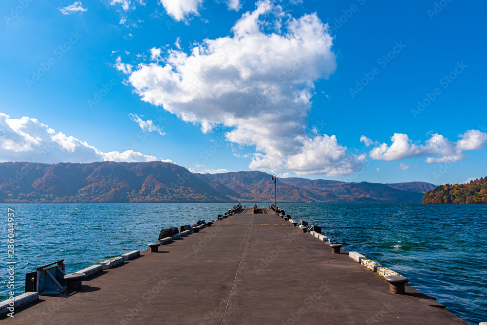 Beautiful view from Lake Towada lakeside pier, clear sky with blue water and white cloud in sunny day during autumn foliage season. Towada hachimantai National Park, Aomori Prefecture, Japan