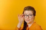 girl with glasses looking at the camera on a yellow background.