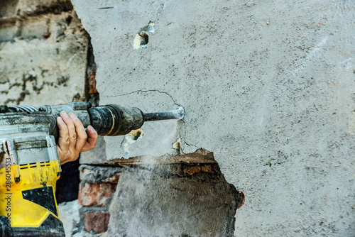 A man with a jackhammer makes an opening in the wall.