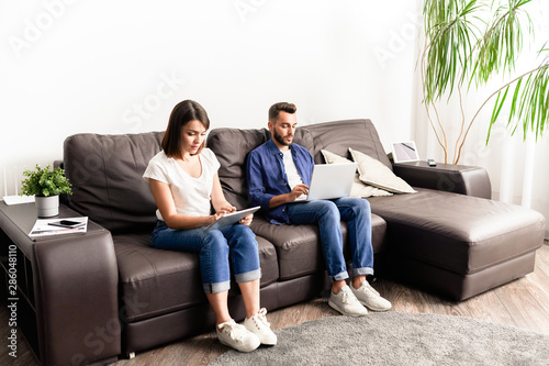 Concentrated young couple in casual clothing sitting on comfortable sofa