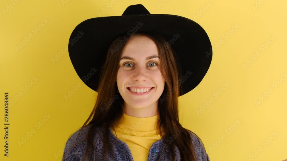 Smiling ginger woman in blue sweater puts on her hat, smiles gladfully, isolated on yellow background. Caucasian woman poses indoor Smiling ginger woman in blue sweater puts on her hat, smiles gladfully, isolated on yellow background. Caucasian woman poses indoor