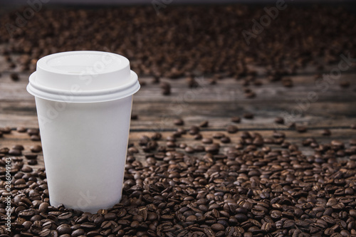 White takeaway cup of coffee with beans on brown wooden table