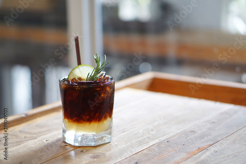 Iced coffee with lemon - A glass of espresso shot mixed with lemonade juice and honey, topped with sliced lime and rosemary leaves on blurred background and copy space, Perfect drink for summer time. photo