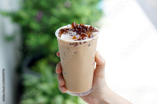 Bubble Milk Tea - Holding a plastic glass of assam milk tea with pearl konjac brown sugar on blurred background, Taiwanese drinking culture.