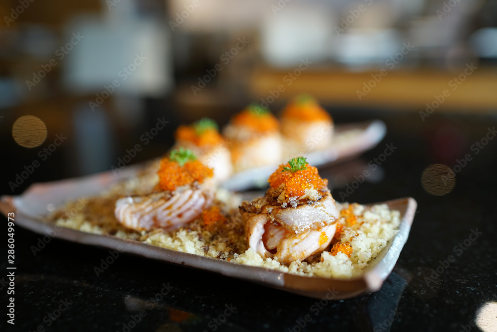 Salmon sushi roll topped with sweet sauce and ebiko roe (Capelin fish caviar) served with crunchy tempura flakes, Traditional Japanese Food. Salmon sushi roll topped with sweet sauce and ebiko roe (Capelin fish caviar) served with crunchy tempura flakes, Traditional Japanese Food.