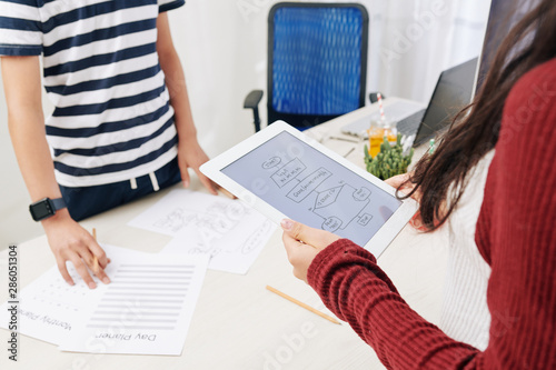 Block scheme on screen of tablet computer in hands of teenage girl talking to classmate and dicussing project photo