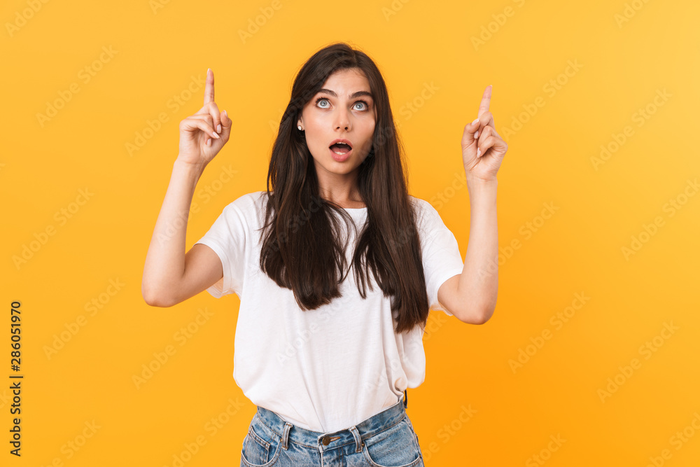 Image of surprised brunette woman with long hair looking upward and pointing fingers at copyspace Image of surprised brunette woman with long hair looking upward and pointing fingers at copyspace