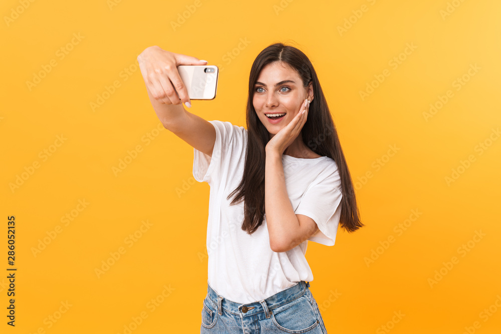 Image of gorgeous brunette woman smiling at camera while taking selfie photo on cellphone Image of gorgeous brunette woman smiling at camera while taking selfie photo on cellphone
