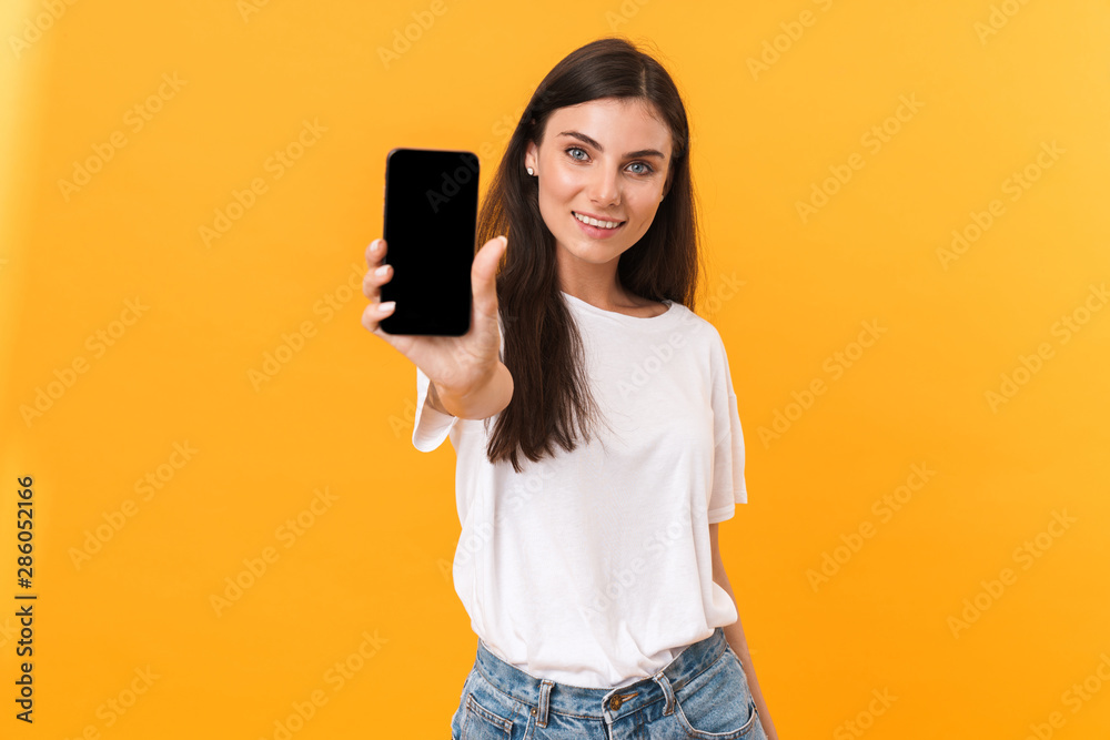 Image of attractive brunette woman wearing basic clothes smiling and showing cellphone screen at camera Image of attractive brunette woman wearing basic clothes smiling and showing cellphone screen at camera