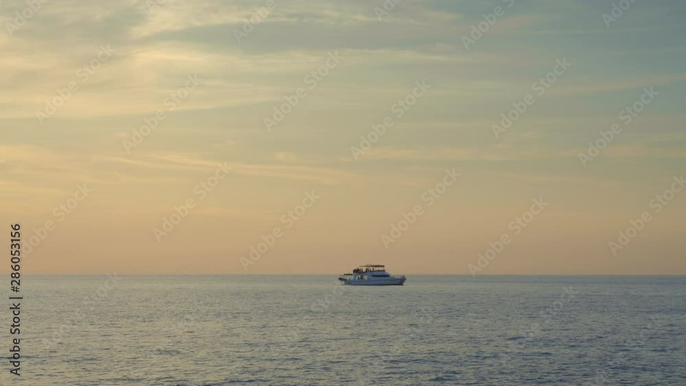 A small two decks boat with people is floating in calm sea with small waves during warm sunset A small two decks boat with people is floating in calm sea with small waves during warm sunset