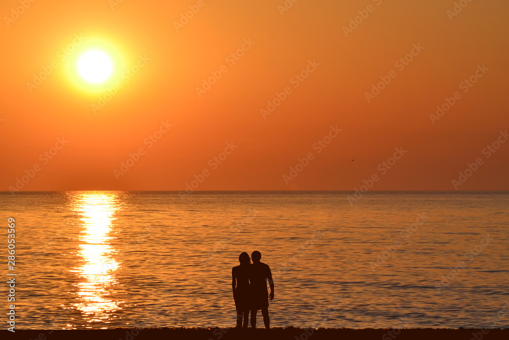 Silhouettes of romantic hugging couple on the beach at sunrise