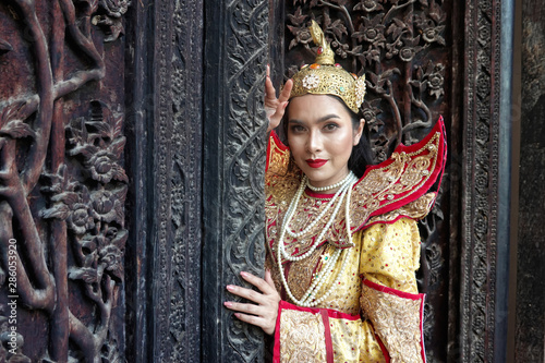 Portrait of an Asian Women in Mandalay, Myanmar Woman with golden Traditional Clothes are Standing Against Art Carving Wooden Door.