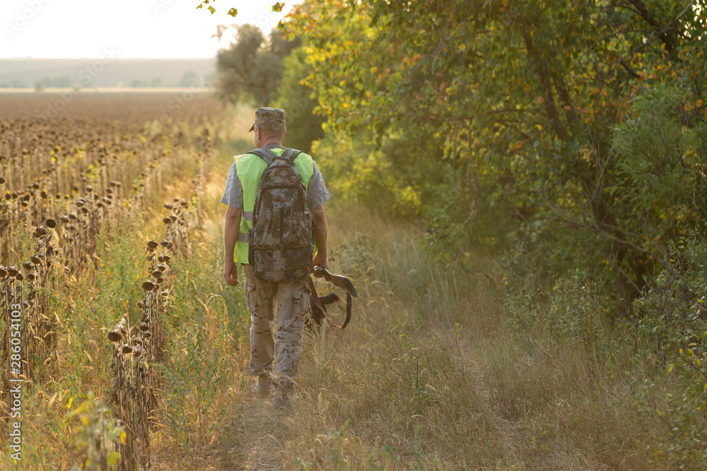 Hunting period, autumn season open. A hunter with a gun in his hands in hunting clothes in the autumn forest in search of a trophy. A man stands with weapons and hunting dogs tracking down the game. Hunting period, autumn season open. A hunter with a gun in his hands in hunting clothes in the autumn forest in search of a trophy. A man stands with weapons and hunting dogs tracking down the game.