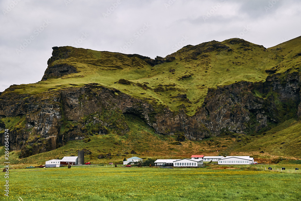 Volcanic mountains in Iceland. Farm in the field near the mountains. 