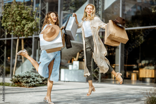 Two happy girlfriends jumpinh with shopping bags in front of the shopping mall outdoors, feeling excited with new purchases photo